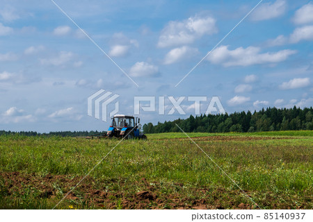 Tractor working in the field, plowing the land, preparing for sowing. View of the field and tractor in the distance against a blue sky with clouds 85140937
