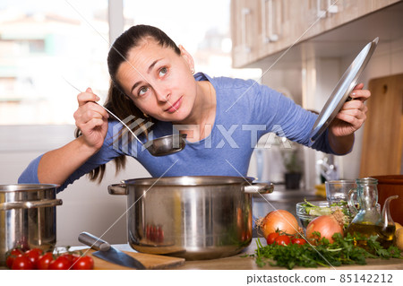 Positive woman holding cooking pot on kitchen Positive woman holding cooking pot on kitchen 85142212