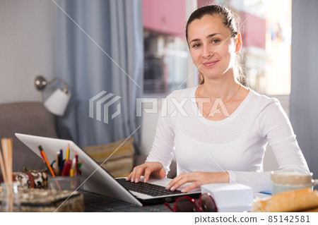 Smiling girl sitting at table at home calculating domestic finances and bills Smiling girl sitting at table at home calculating domestic finances and bills 85142581