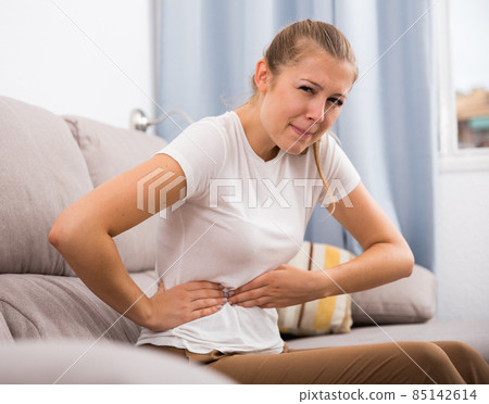 Girl is sitting unhappy because she has a stomach ache Girl is sitting unhappy because she has a stomach ache 85142614