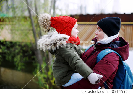 Young mother holding her daughter on hands, walking outdoors Young mother holding her daughter on hands, walking outdoors 85145501