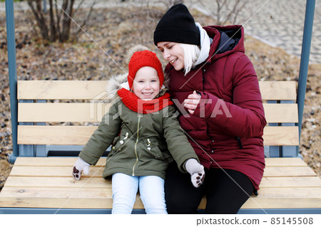 Young mother talking to her cute little daughter outdoors sitting together Young mother talking to her cute little daughter outdoors sitting together 85145508