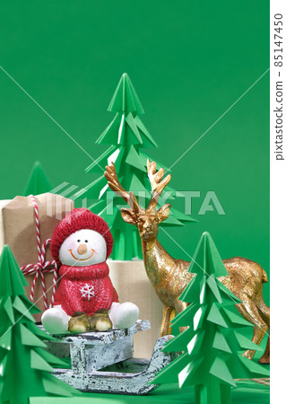 Christmas Scene. Christmas snowman with Gift on wooden sled. Green origami fir tree on a green background. Christmas tree paper cutting design card. 85147450