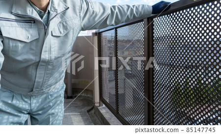 A worker inspecting a handrail on the balcony of an apartment. 85147745