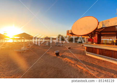 Beach with deck chairs, parasol, and bar during sunrise Beach with deck chairs, parasol, and bar during sunrise 85148119