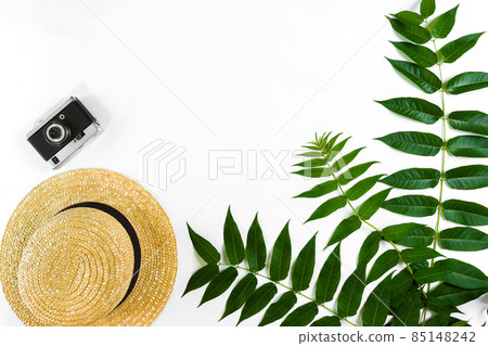Straw hat with green leaves and old camera on white background, Summer background. Top view 85148242