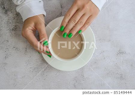 Manicured female hands with stylish green nails holding cup of coffee. Take a break for coffee latte. Trendy modern design manicure. Gel nails. Skin care. Beauty. Nail care Manicured female hands with stylish green nails holding cup of coffee. Take a break for coffee latte. Trendy modern design manicure. Gel nails. Skin care. Beauty. Nail care 85149444