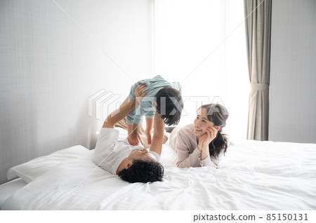 A happy young family with a beautiful mom and a family in a large white bedroom like a new building A happy young family with a beautiful mom and a family in a large white bedroom like a new building 85150131