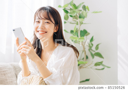 A woman sitting on the sofa and using a smartphone A woman sitting on the sofa and using a smartphone 85150526