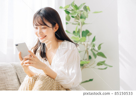 Woman sitting on a sofa and looking at a smartphone 85150533