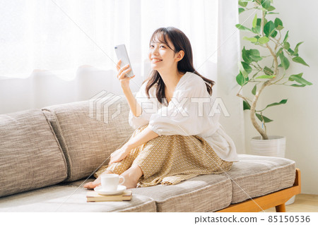 Woman sitting on a sofa and looking at a smartphone 85150536