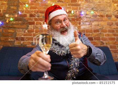 Emotional old bearded man sitting at home and celebrates New Year with friends and family by means of video call. 85151575
