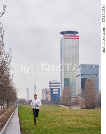 Adult Man running in the parc in winter with city background Adult Man running in the parc in winter with city background 85152586