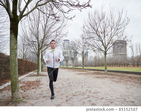 Adult Man running in the parc in winter with city background 85152587