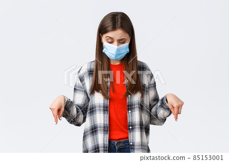 Coronavirus outbreak, leisure on quarantine, social distancing and emotions concept. Hesitant and unsure attractive woman in medical mask, looking down, pointing at strange thing Coronavirus outbreak, leisure on quarantine, social distancing and emotions concept. Hesitant and unsure attractive woman in medical mask, looking down, pointing at strange thing 85153001