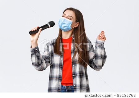 Coronavirus outbreak, leisure on quarantine, social distancing and emotions concept. Carefree young girl in medical mask, singing with microphone, close eyes, enjoying karaoke 85153768