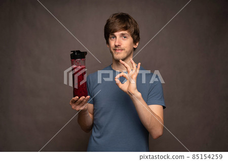 Young man with smoothie on grey background Young man with smoothie on grey background 85154259