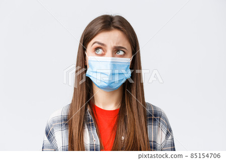 Coronavirus outbreak, leisure on quarantine, social distancing and emotions concept. Intrigued and hesitant young woman in medical mask, looking upper left corner reluctant, white background Coronavirus outbreak, leisure on quarantine, social distancing and emotions concept. Intrigued and hesitant young woman in medical mask, looking upper left corner reluctant, white background 85154706