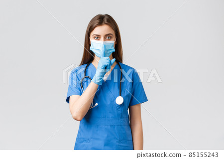 Covid-19, preventing virus, health, healthcare workers and quarantine concept. Keep voice down. Serious female nurse in blue scrubs, medical mask and gloves, shushing, press finger to lips Covid-19, preventing virus, health, healthcare workers and quarantine concept. Keep voice down. Serious female nurse in blue scrubs, medical mask and gloves, shushing, press finger to lips 85155243