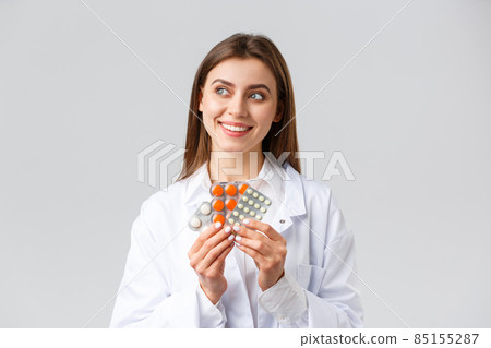 Pharmacy, healthcare workers, insurance and hospitals concept. Thoughtful smiling and pleased female doctor in white scrubs, look away thinking, holding medicine, pills or vitamins Pharmacy, healthcare workers, insurance and hospitals concept. Thoughtful smiling and pleased female doctor in white scrubs, look away thinking, holding medicine, pills or vitamins 85155287