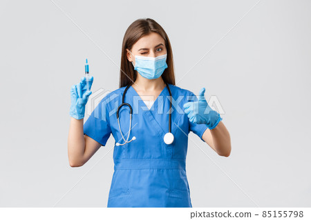 Covid-19, preventing virus, health, healthcare workers and quarantine concept. Friendly female nurse or doctor in blue scurbs, personal protective equipment, wink and assure need make shot of vaccine Covid-19, preventing virus, health, healthcare workers and quarantine concept. Friendly female nurse or doctor in blue scurbs, personal protective equipment, wink and assure need make shot of vaccine 85155798