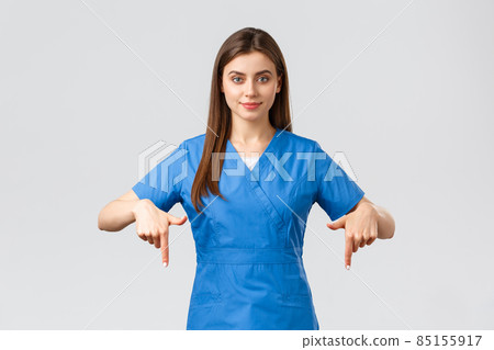 Healthcare workers, prevent virus, insurance and medicine concept. Smiling pretty nurse or doctor in blue scrubs, pointing fingers down, showing patients advertisement, recommend drugstore Healthcare workers, prevent virus, insurance and medicine concept. Smiling pretty nurse or doctor in blue scrubs, pointing fingers down, showing patients advertisement, recommend drugstore 85155917