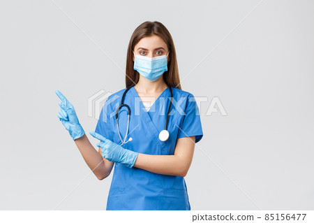 Covid-19, preventing virus, health, healthcare workers and quarantine concept. Pleasant female doctor or nurse in blue scrubs, medical mask and gloves, invite follow page or click link, pointing left Covid-19, preventing virus, health, healthcare workers and quarantine concept. Pleasant female doctor or nurse in blue scrubs, medical mask and gloves, invite follow page or click link, pointing left 85156477