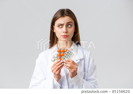 Pharmacy, healthcare workers, insurance and hospitals concept. Thoughtful and skeptical female doctor in white scrubs, look away thinking, consider what pills needed, show medicine 85156620