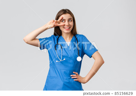 Medical workers, healthcare, covid-19 and vaccination concept. Cheerful and energized young female doctor, pretty nurse in blue scrubs, stethoscope, show peace near eye and smiling upbeat 85156629