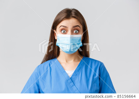 Covid-19, preventing virus, health, healthcare workers and quarantine concept. Surprised female nurse or doctor in blue scrubs and medical mask, staring shocked and excited at camera 85156664