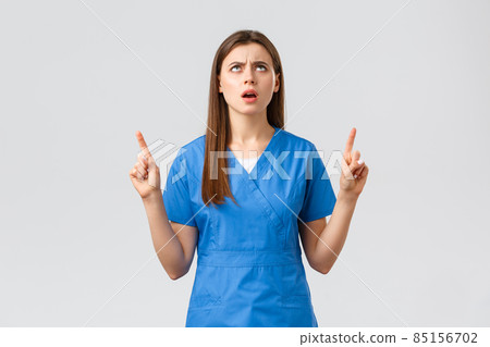 Healthcare workers, prevent virus, insurance and medicine concept. Disappointed and angry female nurse, doctor in blue scrubs, complaining on banner upwards, pointing fingers up, frowning upset Healthcare workers, prevent virus, insurance and medicine concept. Disappointed and angry female nurse, doctor in blue scrubs, complaining on banner upwards, pointing fingers up, frowning upset 85156702