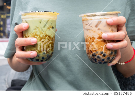 Cropped shot of woman holding a couple cup of iced Bubble tea (Milk tea and Green tea) in her hands. Bubble tea was a traditional drink in Taiwan before it became hugely popular all over the world. 85157496
