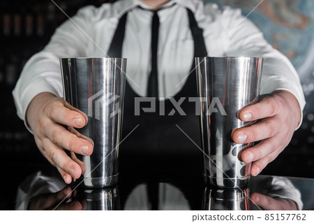 Hands of a professional bartender hold 2 tools for mixing and preparing alcoholic cocktail shakers, close-up Hands of a professional bartender hold 2 tools for mixing and preparing alcoholic cocktail shakers, close-up 85157762