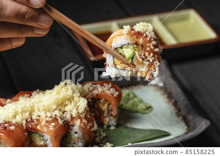 close up of chopsticks in men hands taking portion of sushi roll on the table restaurant / eating sushi roll using chopsticks 85158225