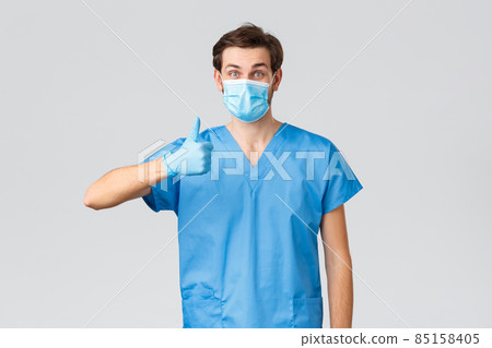Coronavirus outbreak, healthcare workers fighting disease, hospitals concept. Pleased doctor in medical mask, globes and scrubs, show thumb-up to show support, save people lives, treat patients Coronavirus outbreak, healthcare workers fighting disease, hospitals concept. Pleased doctor in medical mask, globes and scrubs, show thumb-up to show support, save people lives, treat patients 85158405