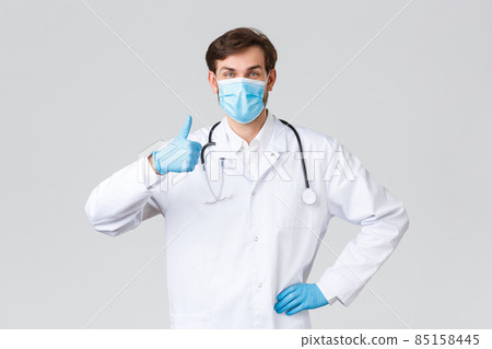 Hospital, healthcare workers, covid-19 treatment concept. Optimistic supportive doctor in medical mask, scrubs and gloves, show thumb-up in approval, like idea, cheer up patient, grey background 85158445