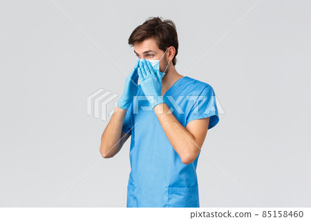 Covid-19, quarantine, hospitals and healthcare workers concept. Serious young doctor enter patient room treating coronavirus symptoms, put on medical mask, scrubs and gloves, grey background Covid-19, quarantine, hospitals and healthcare workers concept. Serious young doctor enter patient room treating coronavirus symptoms, put on medical mask, scrubs and gloves, grey background 85158460