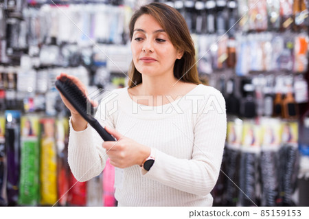 Interested young woman selecting comb for hair in shop Interested young woman selecting comb for hair in shop 85159153
