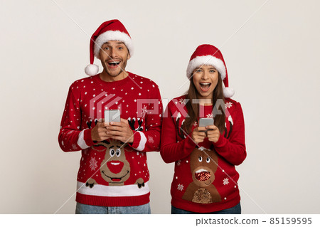 Online Offer. Excited Couple In Santa Hats With Smartphones In Hands 85159595
