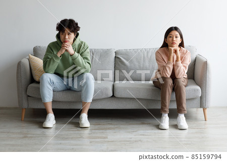 Stubborn young Asian couple sitting on opposite sides of couch in silence after fight, indoors 85159794