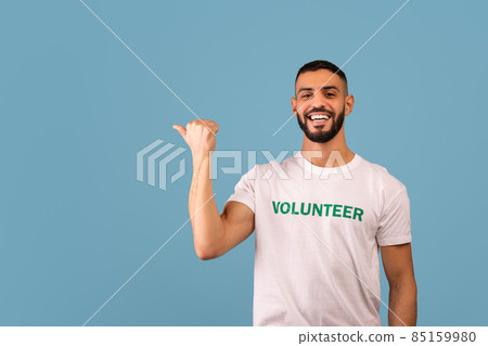 Look there. Happy arab male volunteer pointing aside and smiling, showing empty space, blue background, panorama Look there. Happy arab male volunteer pointing aside and smiling, showing empty space, blue background, panorama 85159980