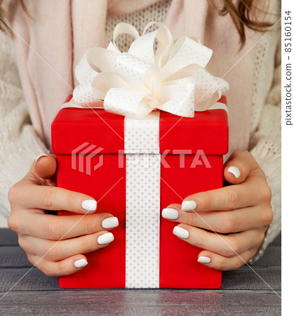 Female hands holding a red gift box with a white ribbon. Christm 85160154