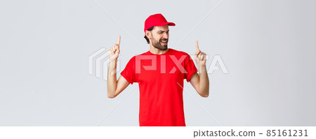 Upbeat handsome bearded delivery guy spending break relaxing, employee in red uniform cap and t-shirt singing song, pointing fingers up carefree, close eyes, standing grey background Upbeat handsome bearded delivery guy spending break relaxing, employee in red uniform cap and t-shirt singing song, pointing fingers up carefree, close eyes, standing grey background 85161231