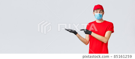 Groceries and packages delivery, covid-19, quarantine and shopping concept. Surprised and excited courier in red uniform, face mask and gloves introduce good new bonus offer, promo, showing banner Groceries and packages delivery, covid-19, quarantine and shopping concept. Surprised and excited courier in red uniform, face mask and gloves introduce good new bonus offer, promo, showing banner 85161259