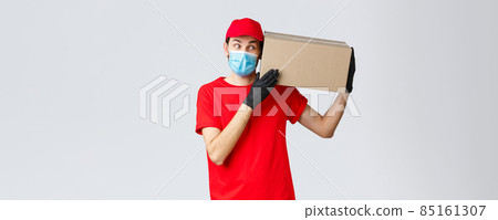 Packages and parcels delivery, covid-19 quarantine delivery, transfer orders. Curious courier in red uniform, gloves and protective face mask, deliver box to client, bring order contactless 85161307