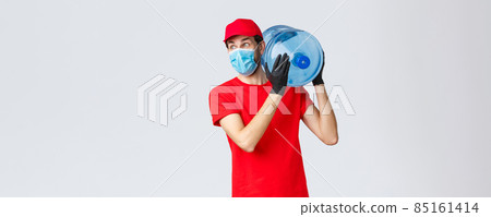 Takeaway, food and groceries delivery, covid-19 contactless orders concept. Excited and impressed courier in red uniform, gloves and face mask, hold bottled water on shoulder, look away astonished 85161414