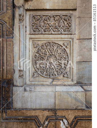 Round floral patterns framed by geometrical patterns carved into the exterior wall of Sultan Hasan Mosque, Cairo, Egypt 85161513