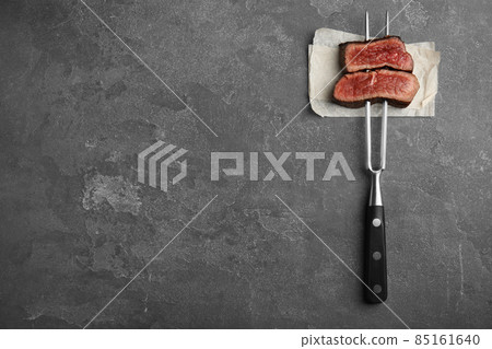 Carving fork with slices of delicious beef steak on grey table, top view. Space for text Carving fork with slices of delicious beef steak on grey table, top view. Space for text 85161640