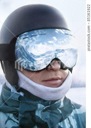 Ski goggles with the reflection of snowed mountains. Man on the background blue sky. Winter Sports. 85161922