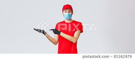 Groceries and packages delivery, covid-19, quarantine and shopping concept. Surprised and excited courier in red uniform, face mask and gloves introduce good new bonus offer, promo, showing banner Groceries and packages delivery, covid-19, quarantine and shopping concept. Surprised and excited courier in red uniform, face mask and gloves introduce good new bonus offer, promo, showing banner 85162979